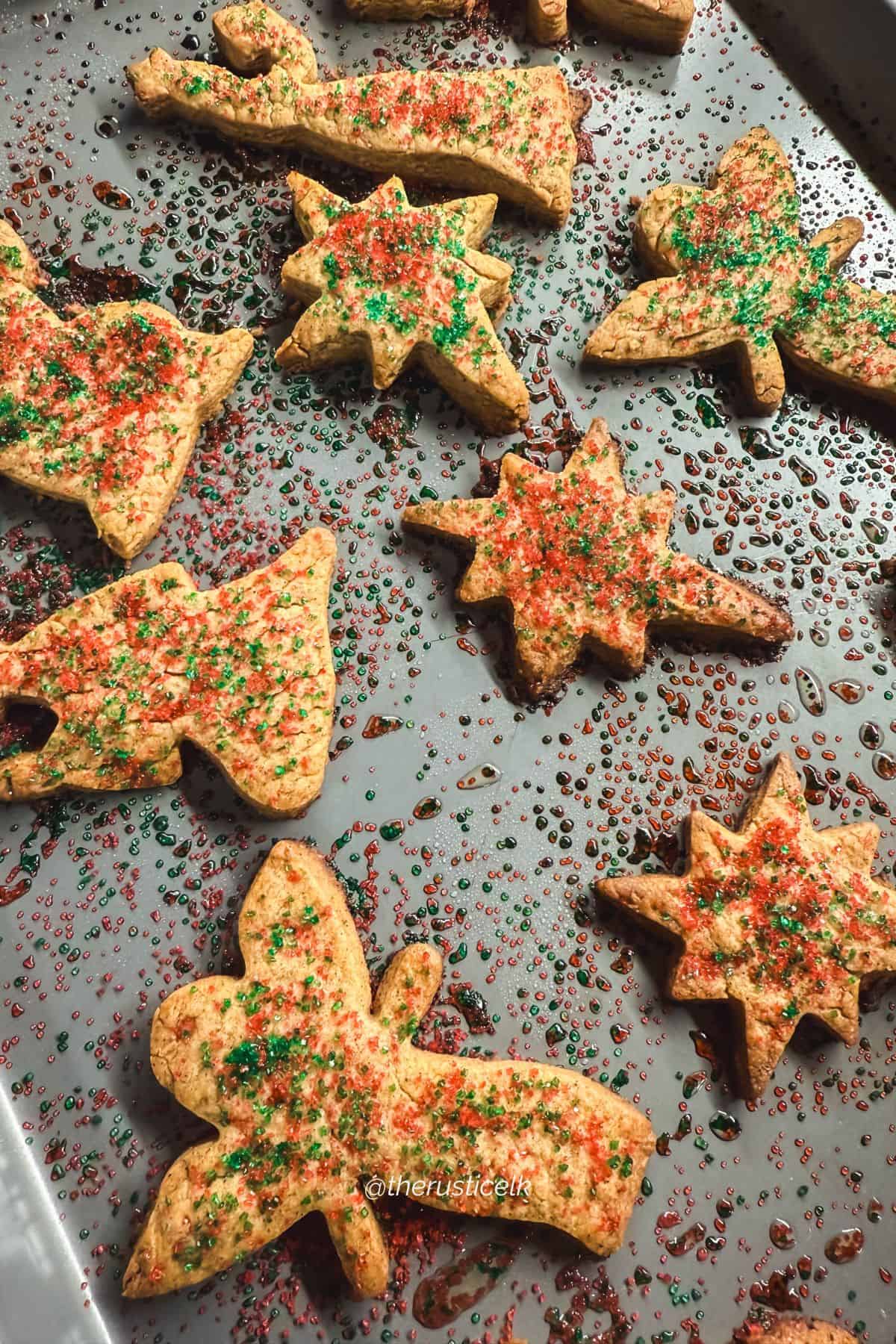 Freshly baked St. Nicholas speculaas cookies on a sheet pan with melted colored sugar, showing crisp edges and texture.