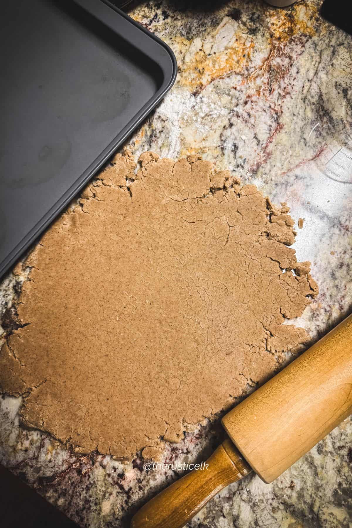 Speculaas cookie dough rolled out on a floured countertop with a wooden rolling pin, ready to cut into shapes.