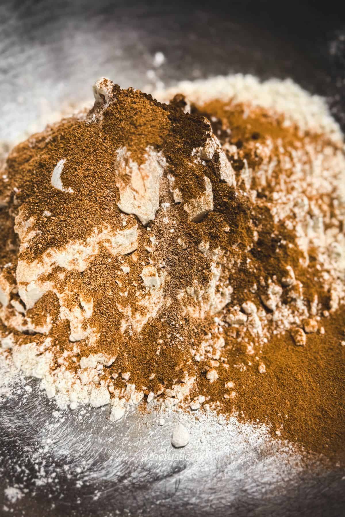 Flour and warm spices—cinnamon, ginger, nutmeg, and cloves—piled together for making traditional speculaas cookies.