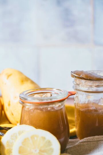 Homemade vanilla cardamom pear butter in glass jars with fresh pears, vanilla beans, and lemon slices on a rustic wooden counter.