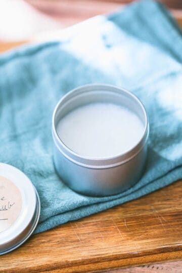 Homemade vapor rub in a small metal tin on a linen towel and wooden cutting board, styled simply with natural light.