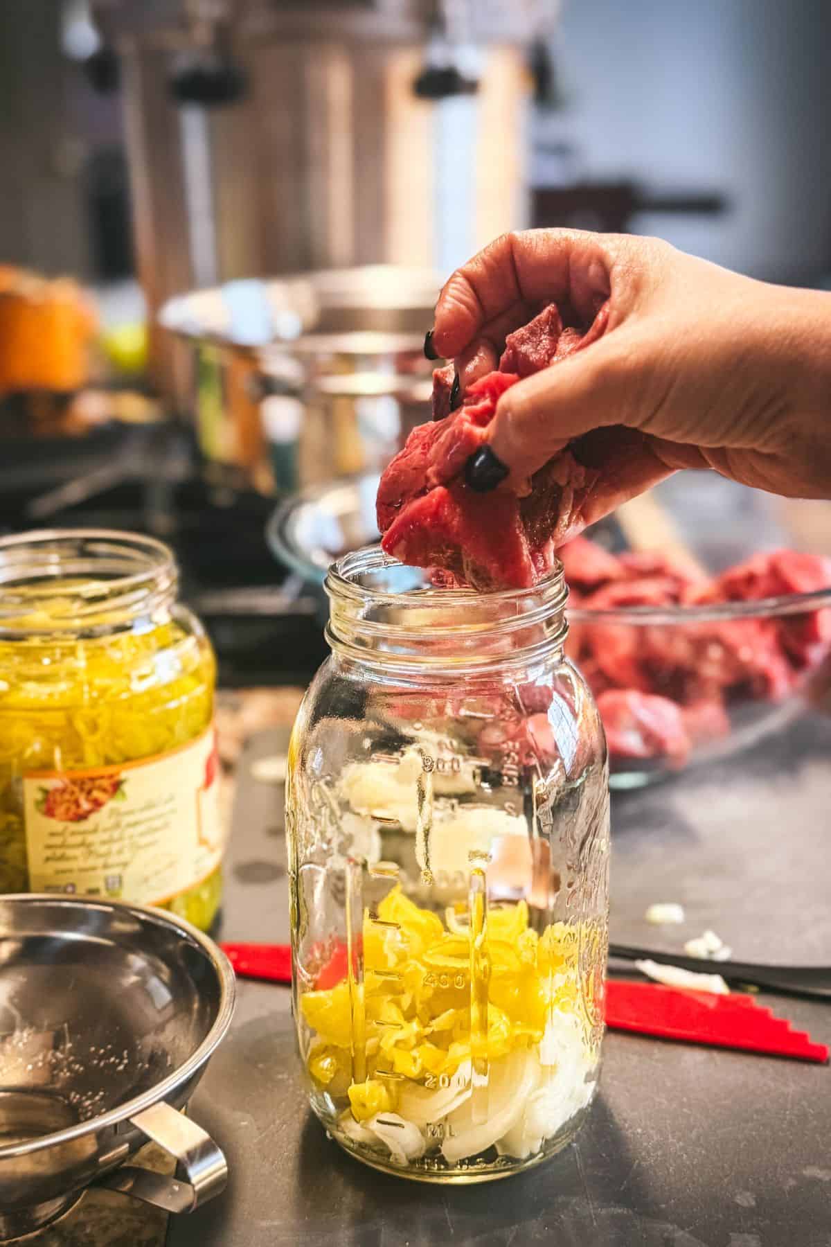 Raw packing beef for Mississippi pot roast with onions, garlic, and pepperoncini peppers in a quart jar