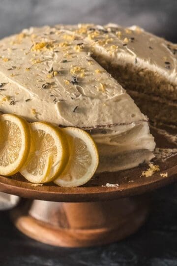 Spring honey cake with lemon buttercream frosting topped with lemon zest and fresh lemon slices on a wooden cake stand.