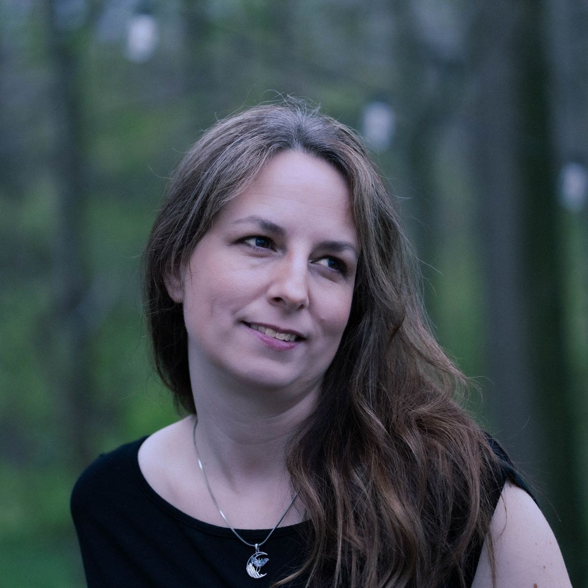 Elle, creator of The Rustic Elk, standing in a forest wearing a black top and moon necklace, looking off to the side.