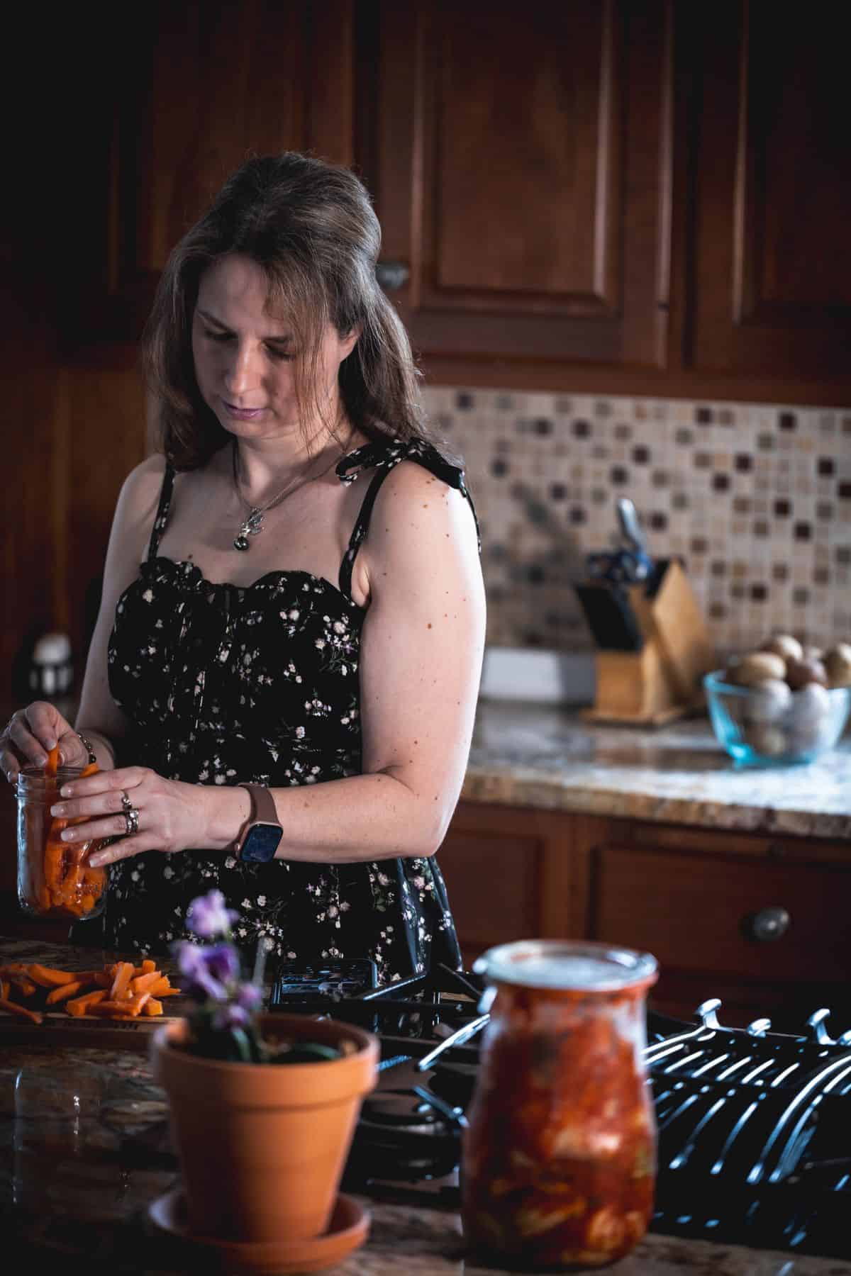 Elle preparing carrots in a home kitchen, placing them into a jar on the counter