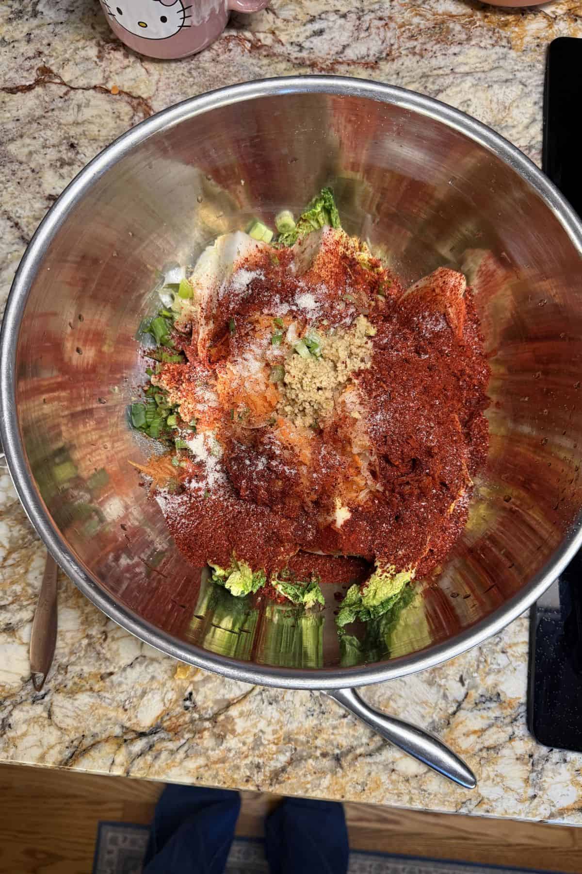 Kimchi ingredients including napa cabbage, garlic, ginger, and chili flakes in a mixing bowl