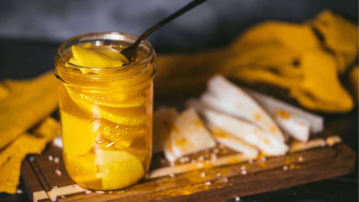 Jar of golden honey pickled daikon radish on wooden board with sliced daikon and spices