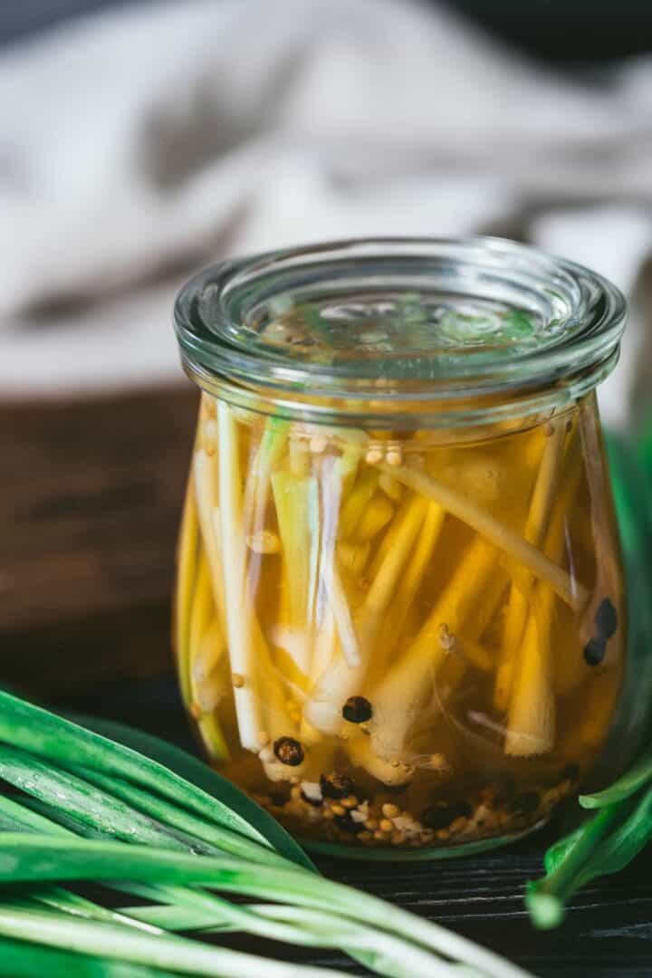 Банка с маринованным диким луком и свежей зеленью на темном фоне
