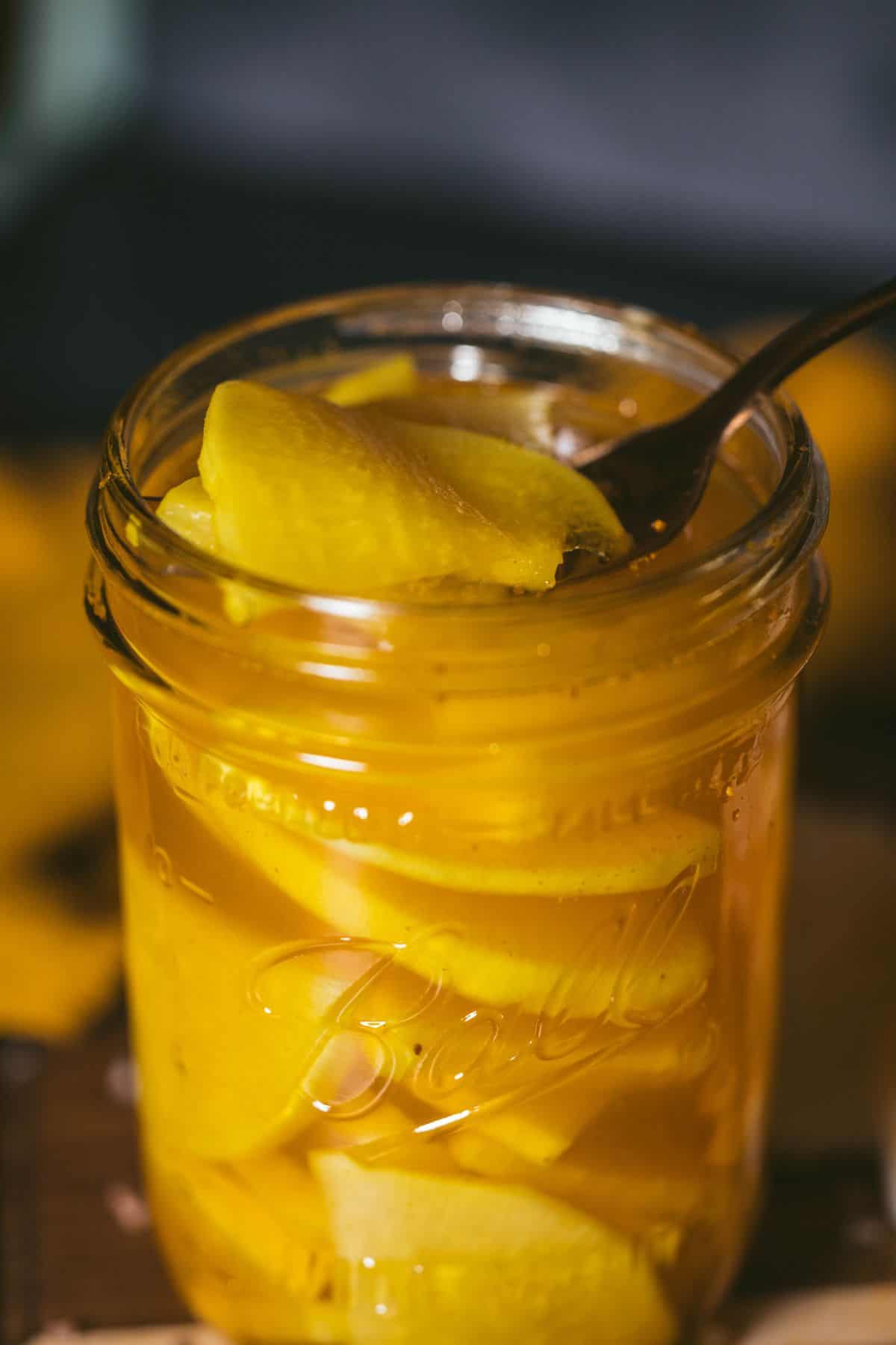 Fork lifting golden pickled daikon radish from glass jar with turmeric brine