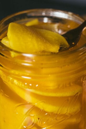 Fork lifting golden pickled daikon radish from glass jar with turmeric brine
