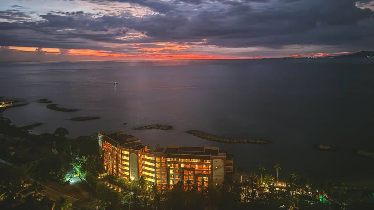 Sunset over Banderas Bay in Puerto Vallarta with glowing resort lights and calm ocean waters beneath a dramatic evening sky.
