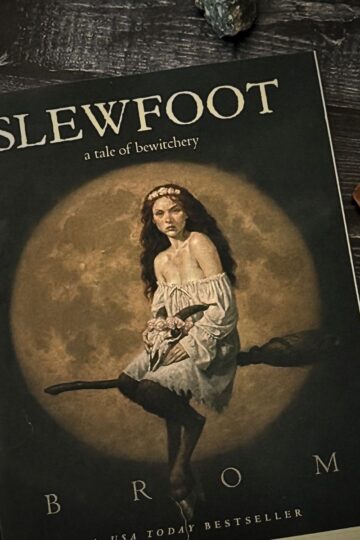 Copy of Slewfoot: A Tale of Bewitchery by Brom resting on a dark wooden surface with witchy decor and moon-themed accents.