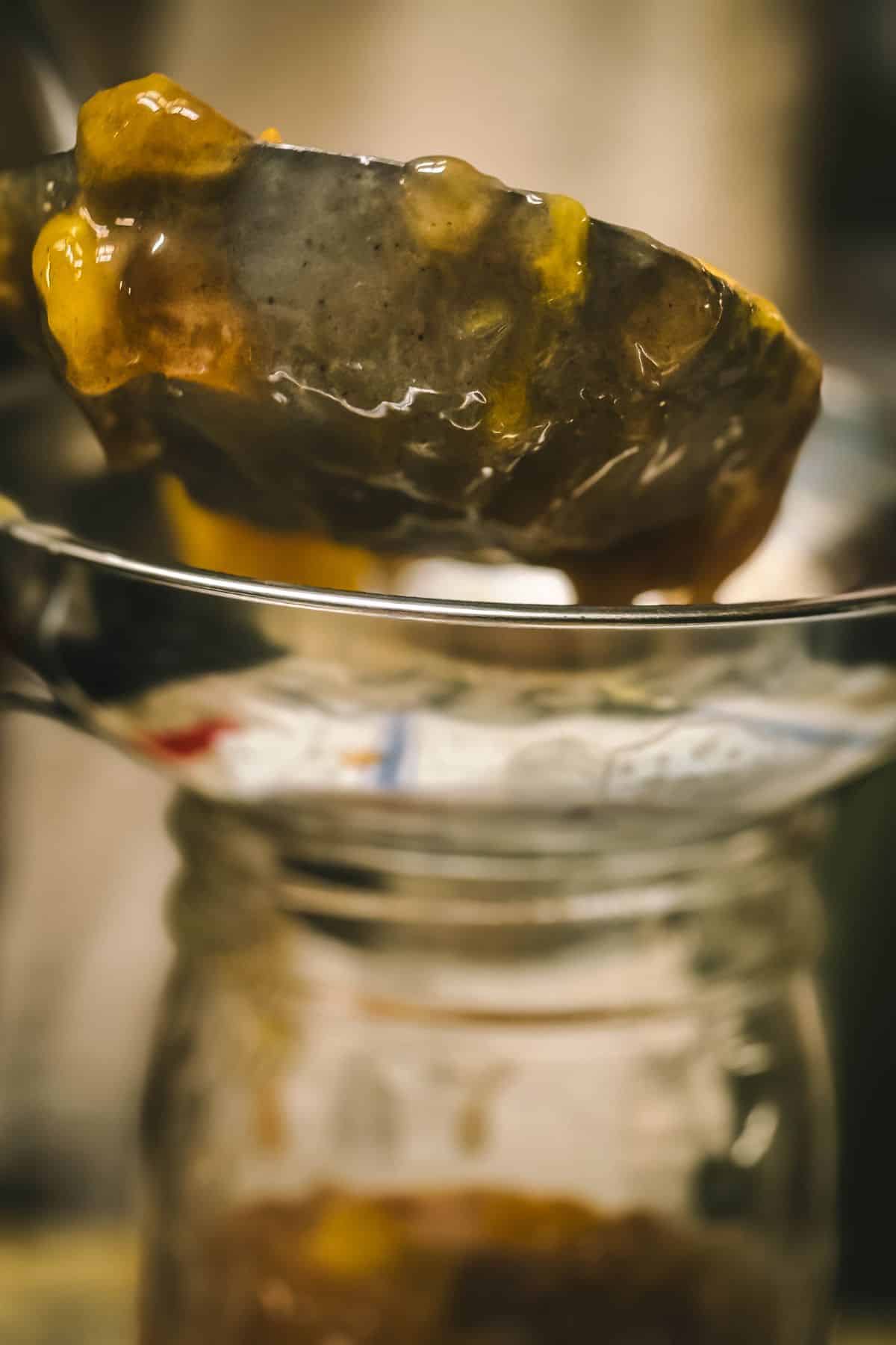Homemade peach pie filling being ladled into a clean canning jar using a wide-mouth funnel before water bath canning.