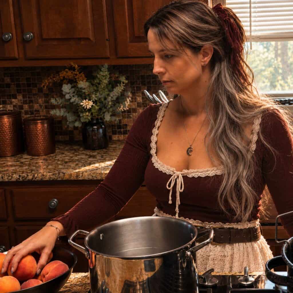 Elle, founder of The Rustic Elk, preparing fresh peaches for preserving in her rustic home kitchen.”